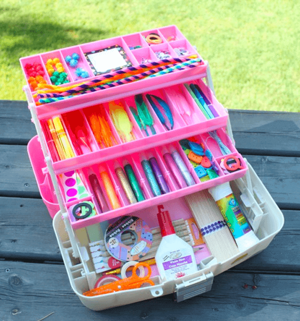 A simple pink box filled with handmade craft supplies on a wooden table.