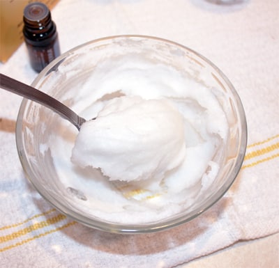 A bowl of coconut oil, a natural ingredient often used in homemade toothpaste recipes, with a spoon in it.