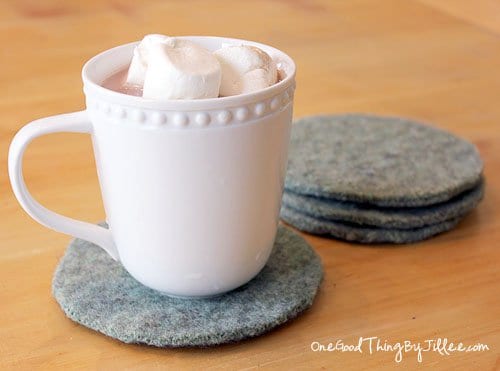 A cup of hot chocolate with marshmallows on top of an old sweater felt coaster.