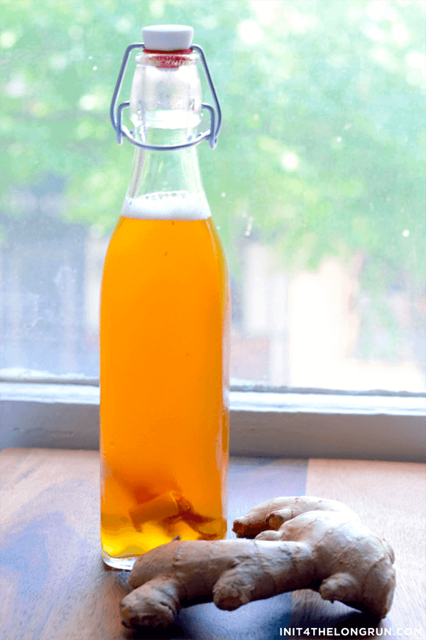 A simple bottle of ginger beer next to a ginger root.