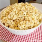 Marshmallow popcorn in a white bowl on a red and white checkered tablecloth.