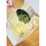 A person making their own herb butter by pouring pesto into a blender.