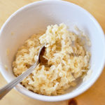 A white bowl filled with rice krispie treats on a wooden table.