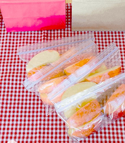 A bag of fresh apples and oranges on a table with a checkered tablecloth.