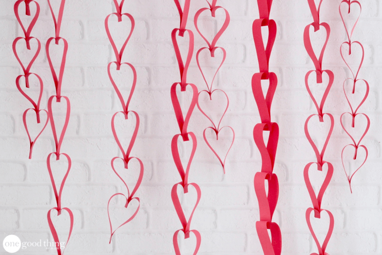 Several finished red paper heart chains hanging against a white brick wall