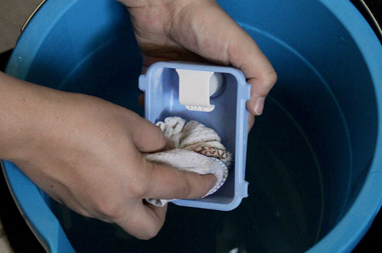 A person holding a blue bucket filled with a plastic container, resembling a miniature washing machine.