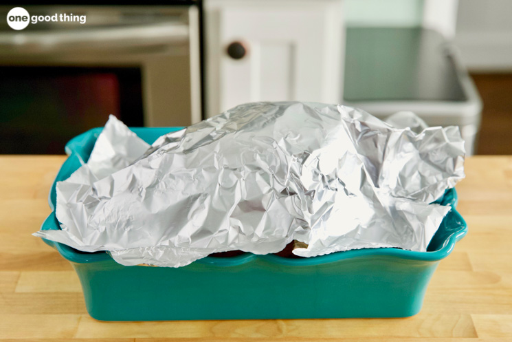 A roasted turkey resting in a green serving dish, covered in aluminum foil