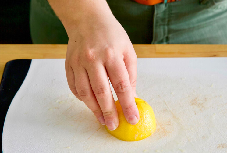 A person cutting a lemon on a cutting board.