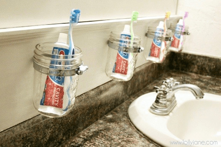 mason jars hanging on a bathroom wall holding toothbrushes and toothpaste