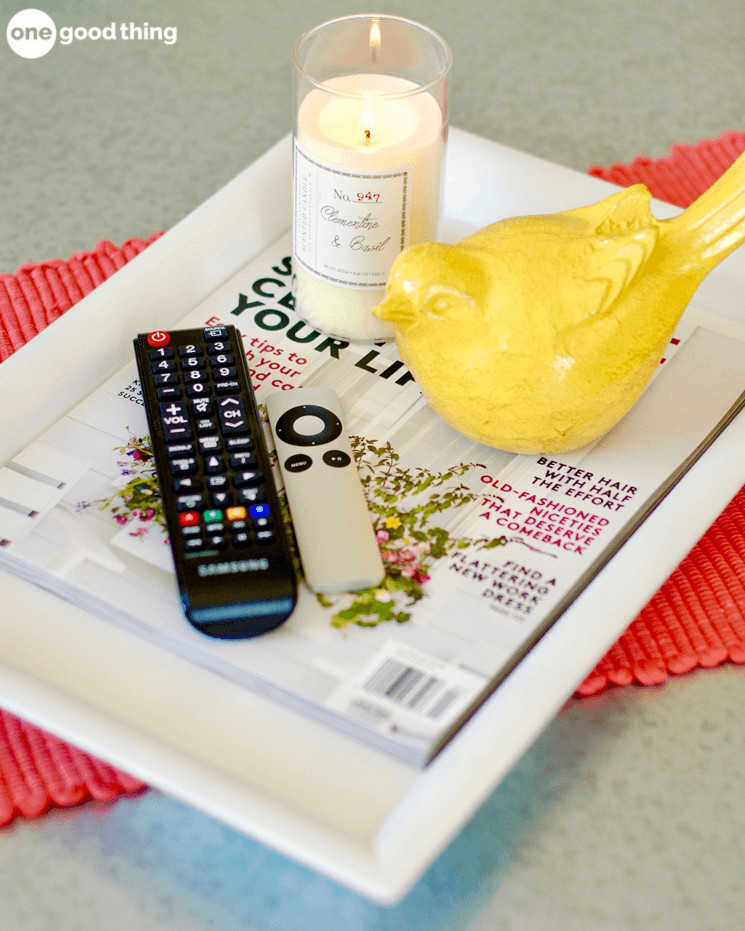 remotes sitting on a tray with magazines and a candle