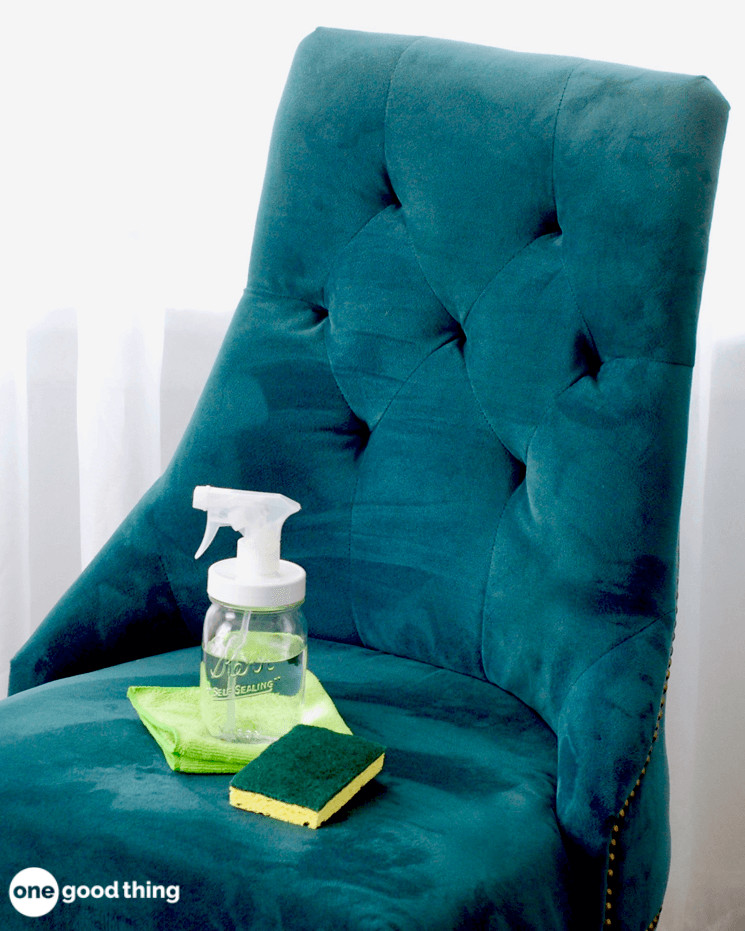 A spray jar full of isopropyl alcohol sitting atop a microfiber cloth and next to a sponge on a green microfiber chair