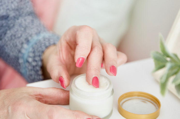 A woman is putting cream into a jar on a table to relieve her everyday aches.