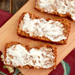 A mat and tray placed on a wooden rack with three slices of Gluten Free Pumpkin Bread and cream cheese spreaded on top.
