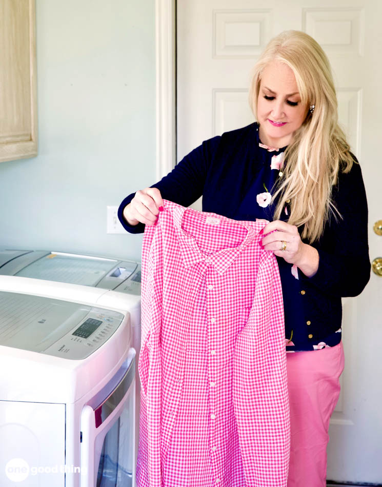 blond woman holding up a red gingham shirt in a laundry room
