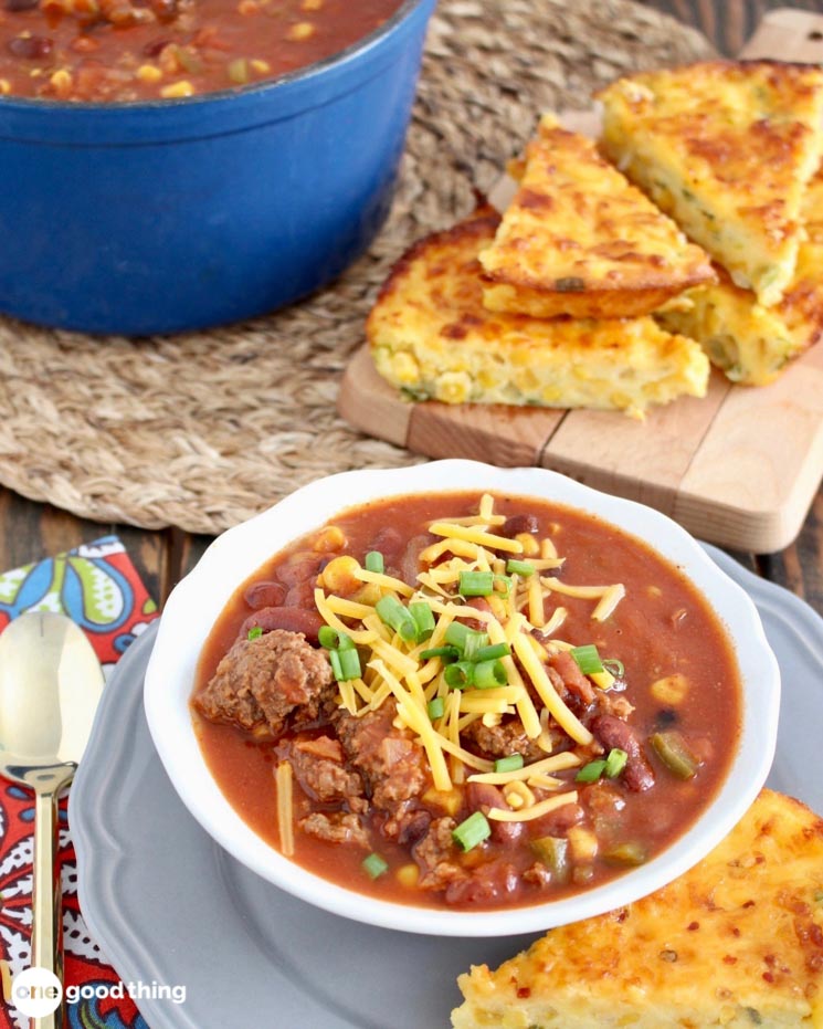 bowl of chili topped with cheese and green onions with cheesy bread on the side