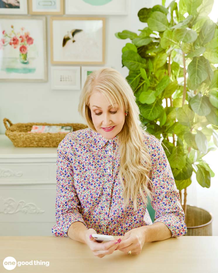 A woman sitting at a table, engrossed in her phone while exploring iPhone hacks.