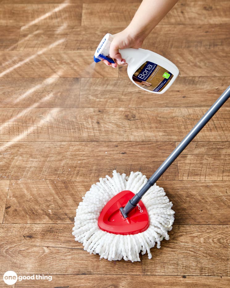 caring for hardwood floors - spraying Bona floor cleaner on a wood floor in front of a mop