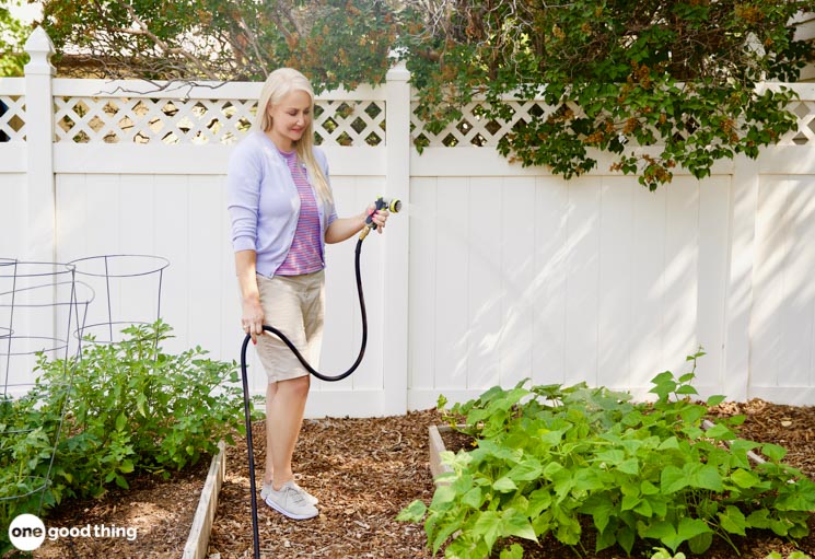 blond woman using a hose to water plants in a garden