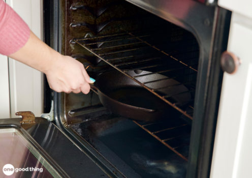 woman's hand putting empty cast iron skillet into oven