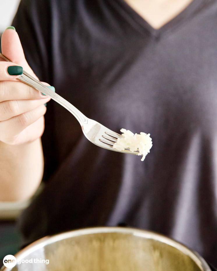 Woman's hand holding a fork with a small amount of rice on the end