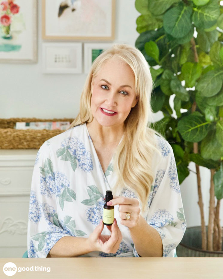 A woman sitting at a table holding a bottle of essential oil.
