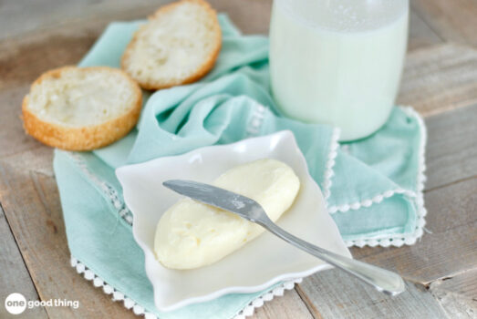 making butter and buttermilk - homemade butter and butter knife on a small square plate, a cut biscuit, and a bottle of buttermilk, all on a light aqua cloth