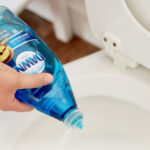 A person using toilet cleaner to unclog a toilet.