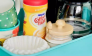A kitchen cart **with a coffee maker, cups,** and mugs.