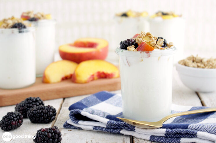 How To Make Homemade Yogurt - homemade yogurt in a glass, topped with granola and fresh berries, with sliced fresh peach and fresh blackberries nearby