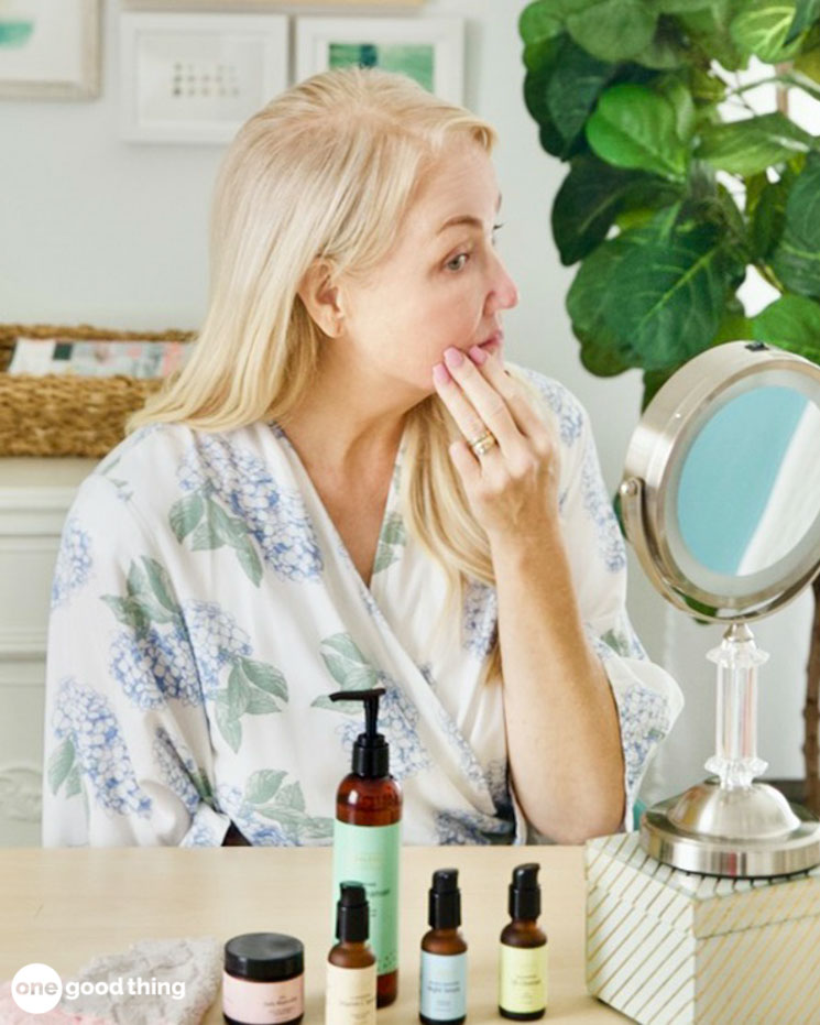 A woman is sitting in front of a mirror, meticulously examining her anti-aging skincare products.