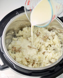 After mashing the instant pot mashed potatoes, add the hot milk and butter, then mash some more until creamy.