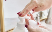 A woman applying foaming hand soap to her hands in front of a mirror.