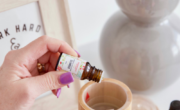 Person dispensing oil from a small bottle into a wooden diffuser, surrounded by other essential oil bottles, with text "7 essential oil mistakes to avoid when using essential oils".