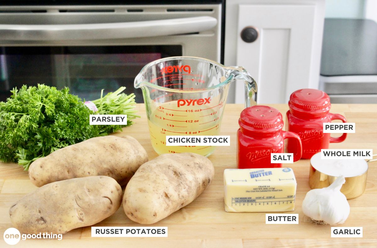 Ingredients for a recipe displayed on a kitchen counter: parsley, chicken stock, salt, pepper, whole milk, garlic, butter, and russet potatoes for creamy instant pot mashed potatoes.