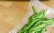 A vacuum-sealed bag of green beans is placed on a wooden surface, labeled "Green Beans" in green ink, showcasing the efficiency of the vacuum sealer.