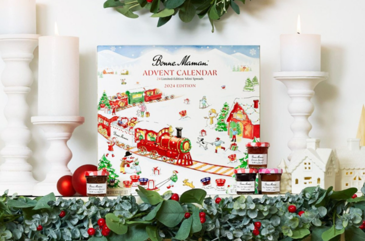 The Bonne Maman Advent Calendar 2024 graces a festively decorated table adorned with twinkling candles, mini jars, and lush greenery.