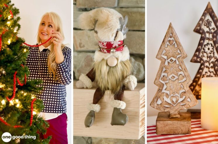 A woman decorates a Christmas tree with holiday decor, including a festive plush reindeer toy and a wooden tree figurine illuminated by the warm glow of a nearby candle.