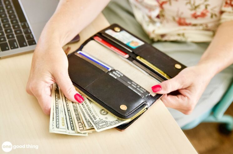 A person holding an open wallet with cash and credit cards next to a laptop on a desk contemplates the budgeting rule.