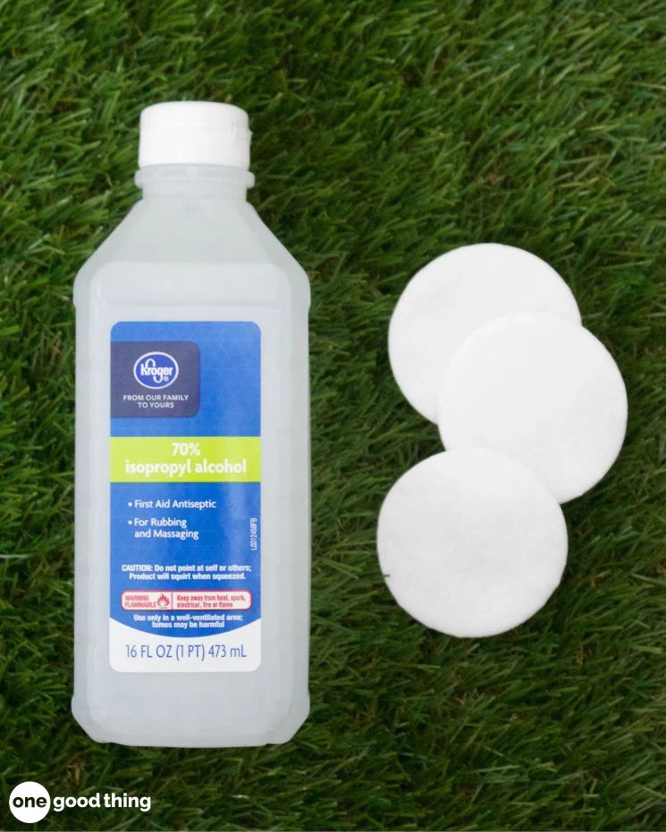 A bottle of 70% isopropyl alcohol and three round cotton pads rest on green grass, ready to soothe mosquito bites.