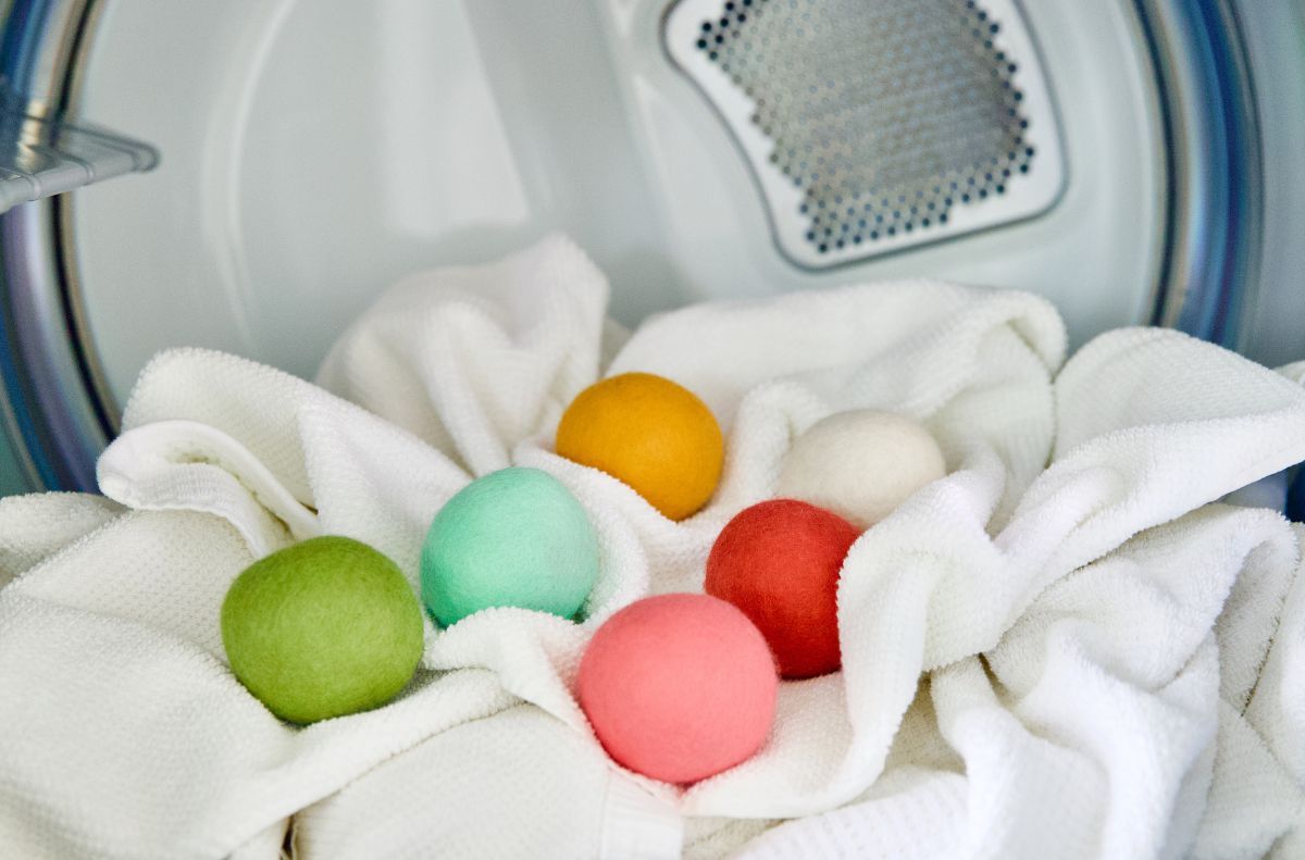 Six colorful wool dryer balls rest on white towels inside an open dryer drum, showcasing the benefits of wool dryer balls for naturally softening fabrics and reducing drying time.