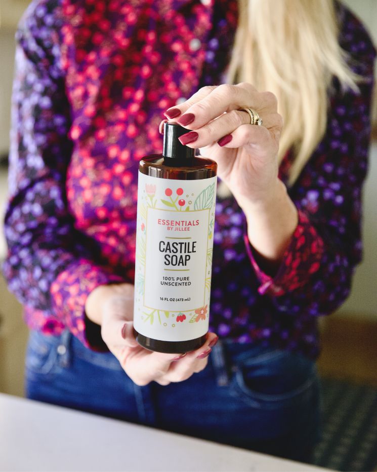 A person with painted nails and a floral shirt holds a bottle of 