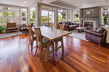 Open-plan living and dining area with wooden floors—easy to maintain with tips on how to clean hardwood floors—a wooden dining table, brown leather sofas, a cozy fireplace, and large windows that fill the space with natural light.