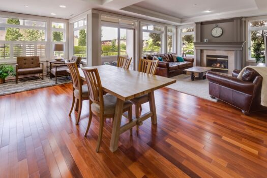 Open-plan living and dining area with wooden floors—easy to maintain with tips on how to clean hardwood floors—a wooden dining table, brown leather sofas, a cozy fireplace, and large windows that fill the space with natural light.