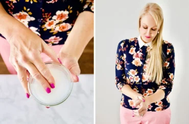 A woman with long blonde hair and pink pants applies homemade arthritis pain relief cream from a small glass bowl onto her wrist, wearing a navy floral top.