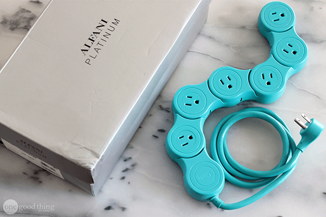 A teal flexible power strip, perfect as a simple charging station, lies on a marble surface next to a silver Alfani Platinum box.