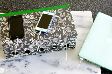 A floral paper-covered tissue box serves as a simple charging station, neatly organizing cables through holes to power two smartphones and a laptop.