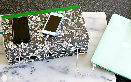 A floral paper-covered tissue box serves as a simple charging station, neatly organizing cables through holes to power two smartphones and a laptop.