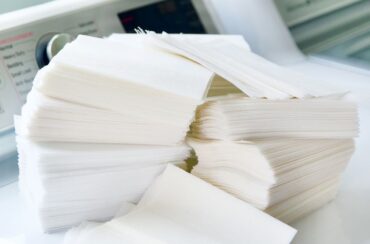 A large stack of white dryer sheets sits on a white surface near a washing machine—reminding you it might be time to ditch the dryer sheets for a more eco-friendly laundry routine.