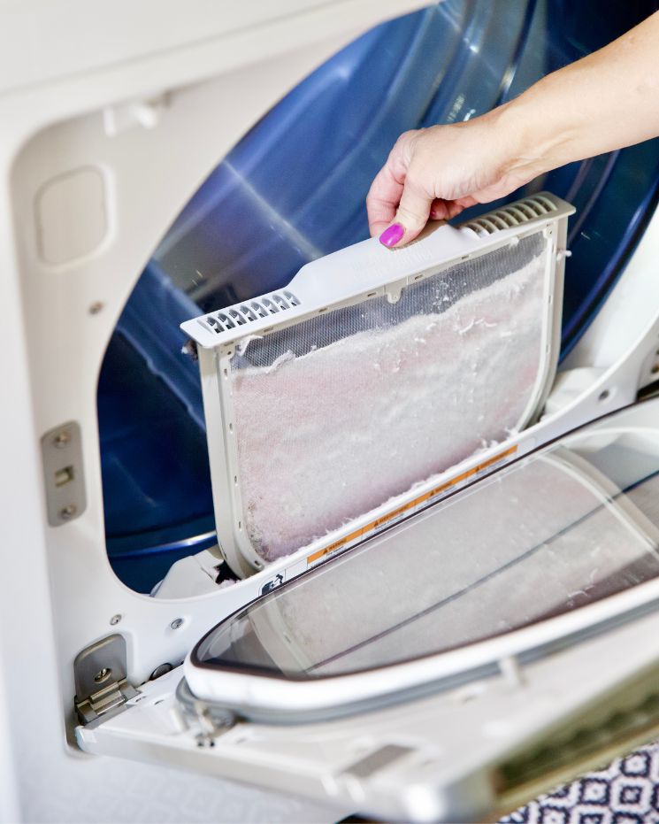 A person removes a lint trap from a clothes dryer. The lint trap is covered with collected lint—even when you use dryer balls to help reduce static and drying time.