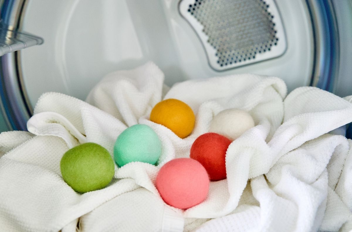Six colorful wool dryer balls rest on white towels inside a clothes dryer, showing how easy it is to use dryer balls for softer, fresher laundry.